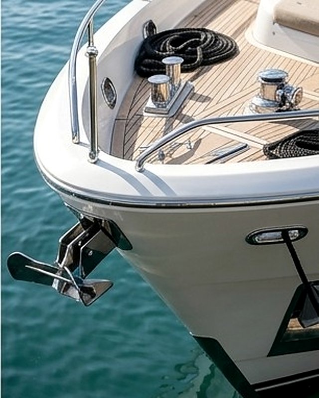 Coiled dock lines and polished stainless cleats on a foredeck above green water